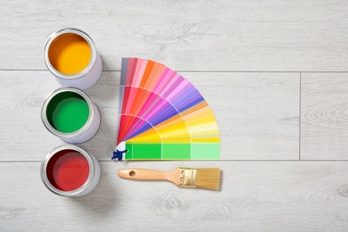 Photo of Flat lay composition with cans of paint, color palette samples and brush on wooden background. Space for text