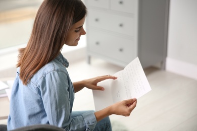 Young woman reading paper letter at home