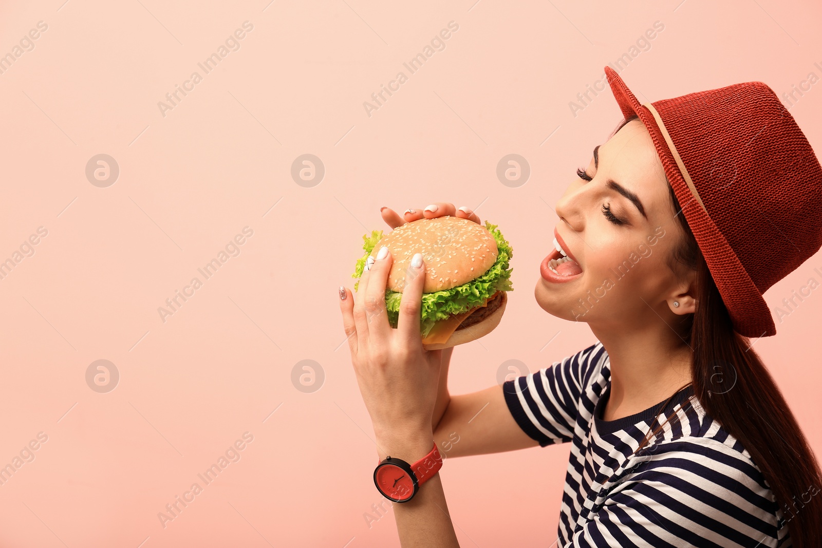 Photo of Young woman eating tasty burger on color background. Space for text