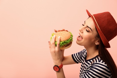 Young woman eating tasty burger on color background. Space for text
