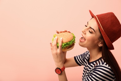 Photo of Young woman eating tasty burger on color background. Space for text