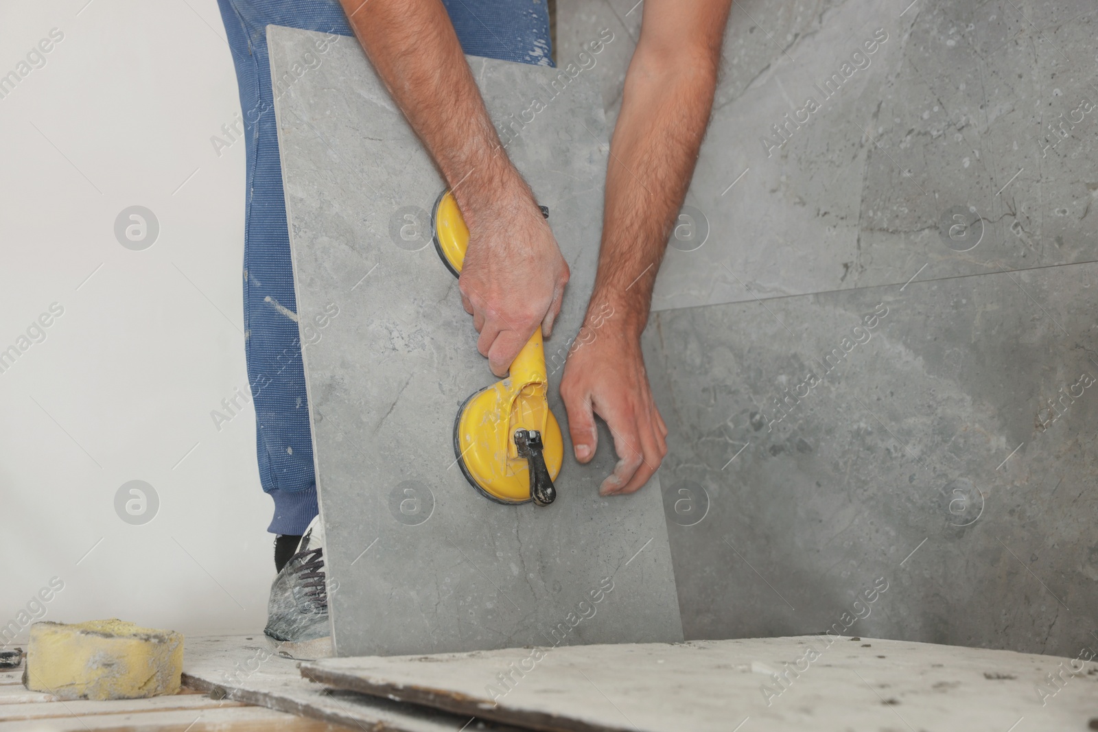 Photo of Worker installing wall tile with vacuum holder indoors, closeup