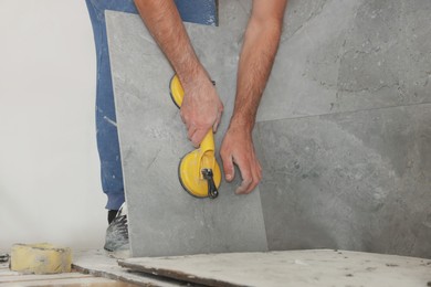 Worker installing wall tile with vacuum holder indoors, closeup