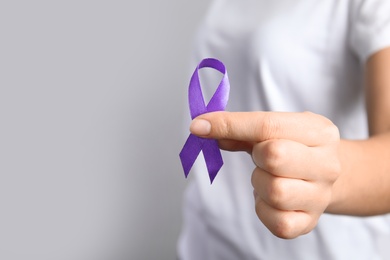 Woman holding purple ribbon on grey background, closeup. Domestic violence awareness