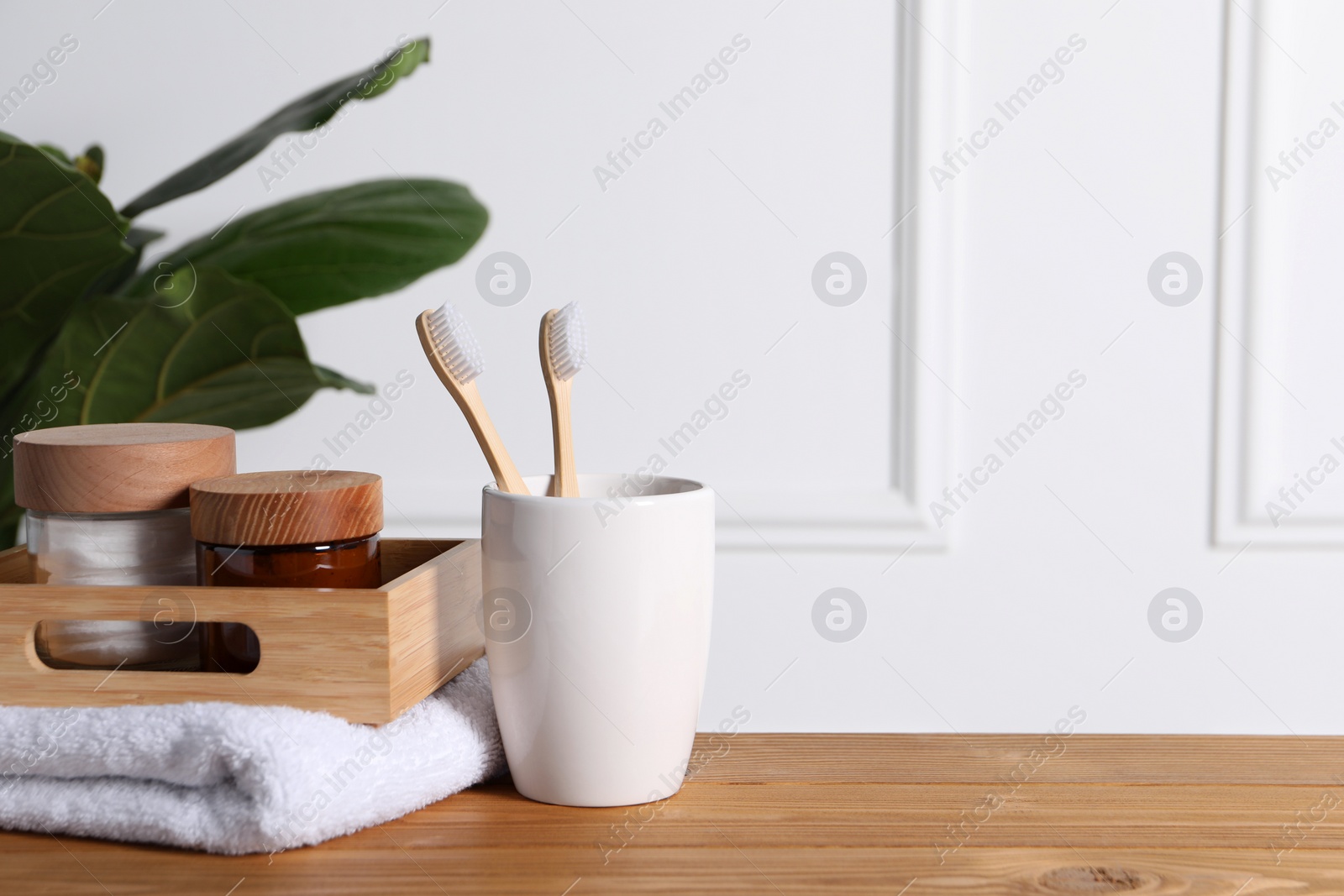 Photo of Bamboo toothbrushes in holder, towel, cosmetic products and leaves on wooden table. Space for text