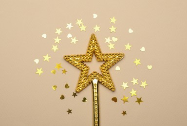 Photo of Beautiful golden magic wand and confetti on beige background, flat lay