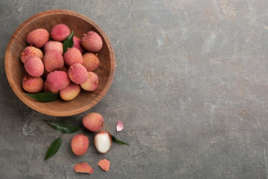 Photo of Fresh ripe lychee fruits in bowl on grey table, flat lay. Space for text