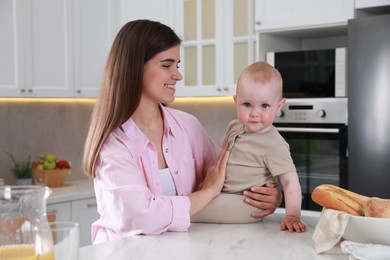 Photo of Happy young woman and her cute little baby spending time together in kitchen