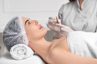 Professional cosmetologist holding skincare ampoule while working with client in clinic, closeup