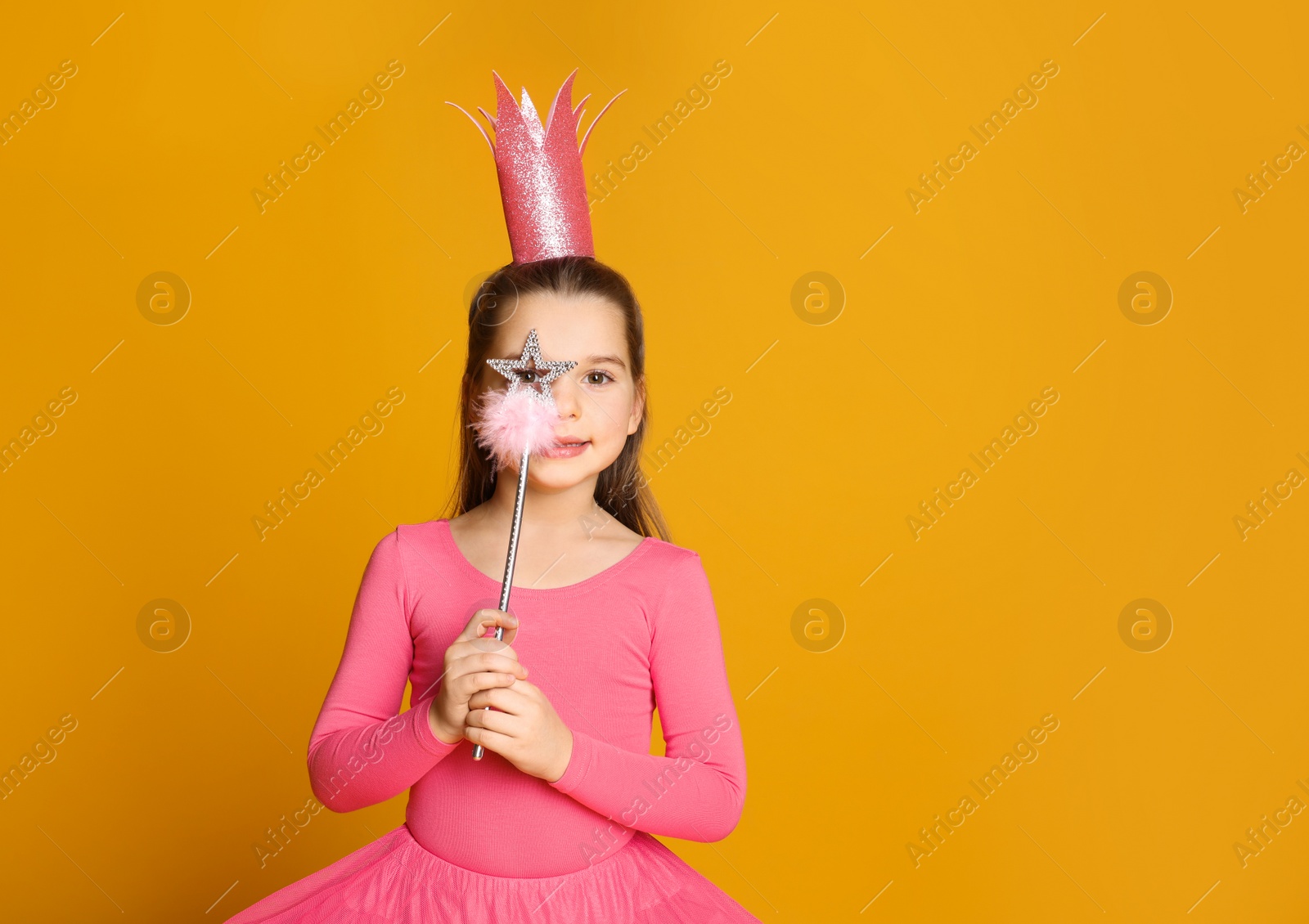 Photo of Cute girl in pink crown with magic wand on yellow background, space for text. Little princess