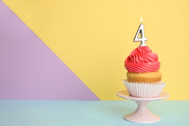 Photo of Birthday cupcake with number four candle on stand against color background, space for text