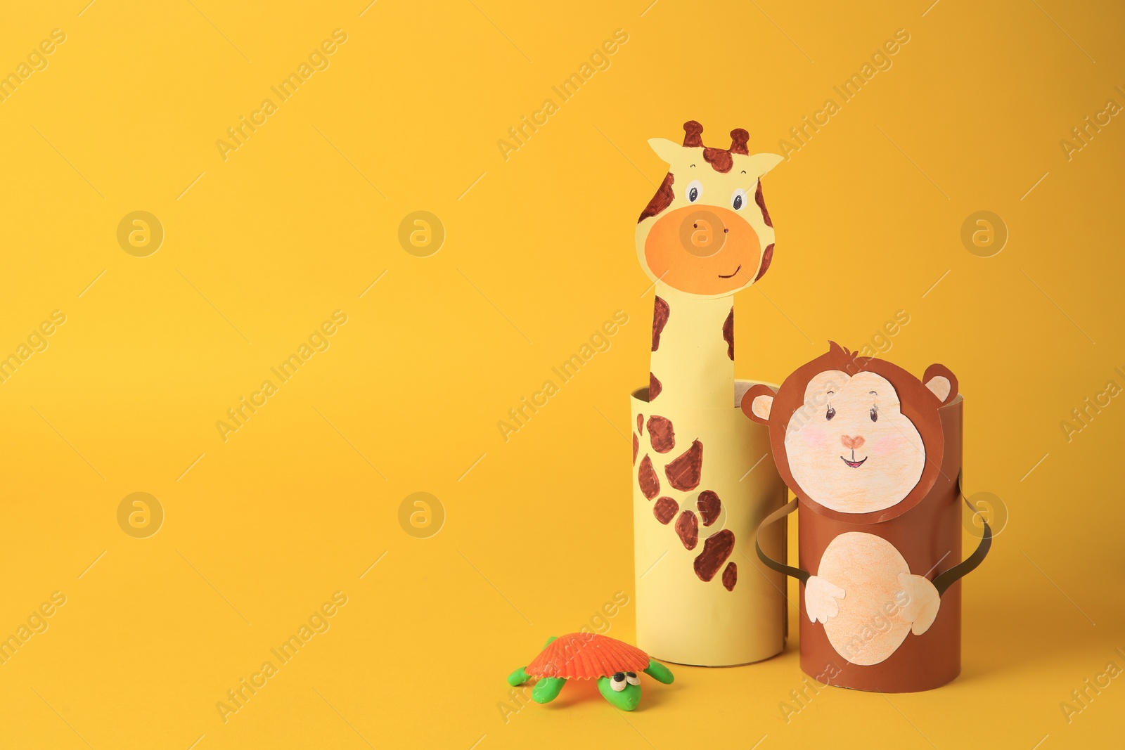 Photo of Toy monkey and giraffe made from toilet paper hubs with plasticine turtle on yellow background, space for text. Children's handmade ideas