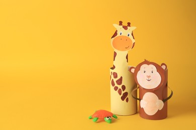 Photo of Toy monkey and giraffe made from toilet paper hubs with plasticine turtle on yellow background, space for text. Children's handmade ideas