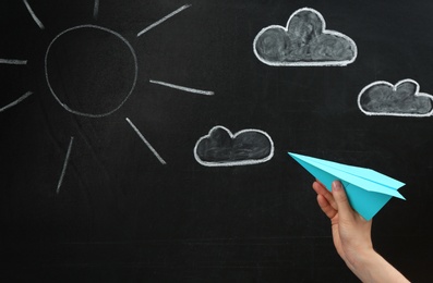 Woman holding paper plane near blackboard, closeup