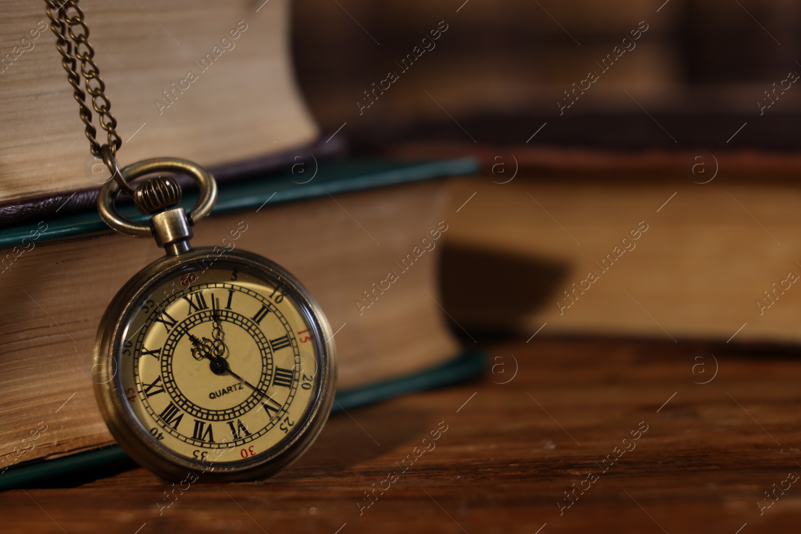 Photo of Pocket clock with chain and books on wooden table, closeup. Space for text