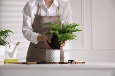 Photo of Woman planting fern at white table indoors, closeup