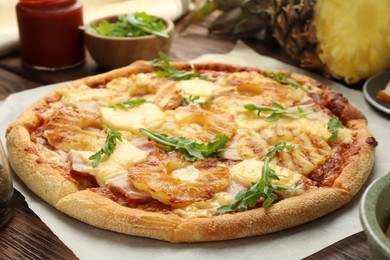 Photo of Delicious pineapple pizza with arugula on wooden table, closeup