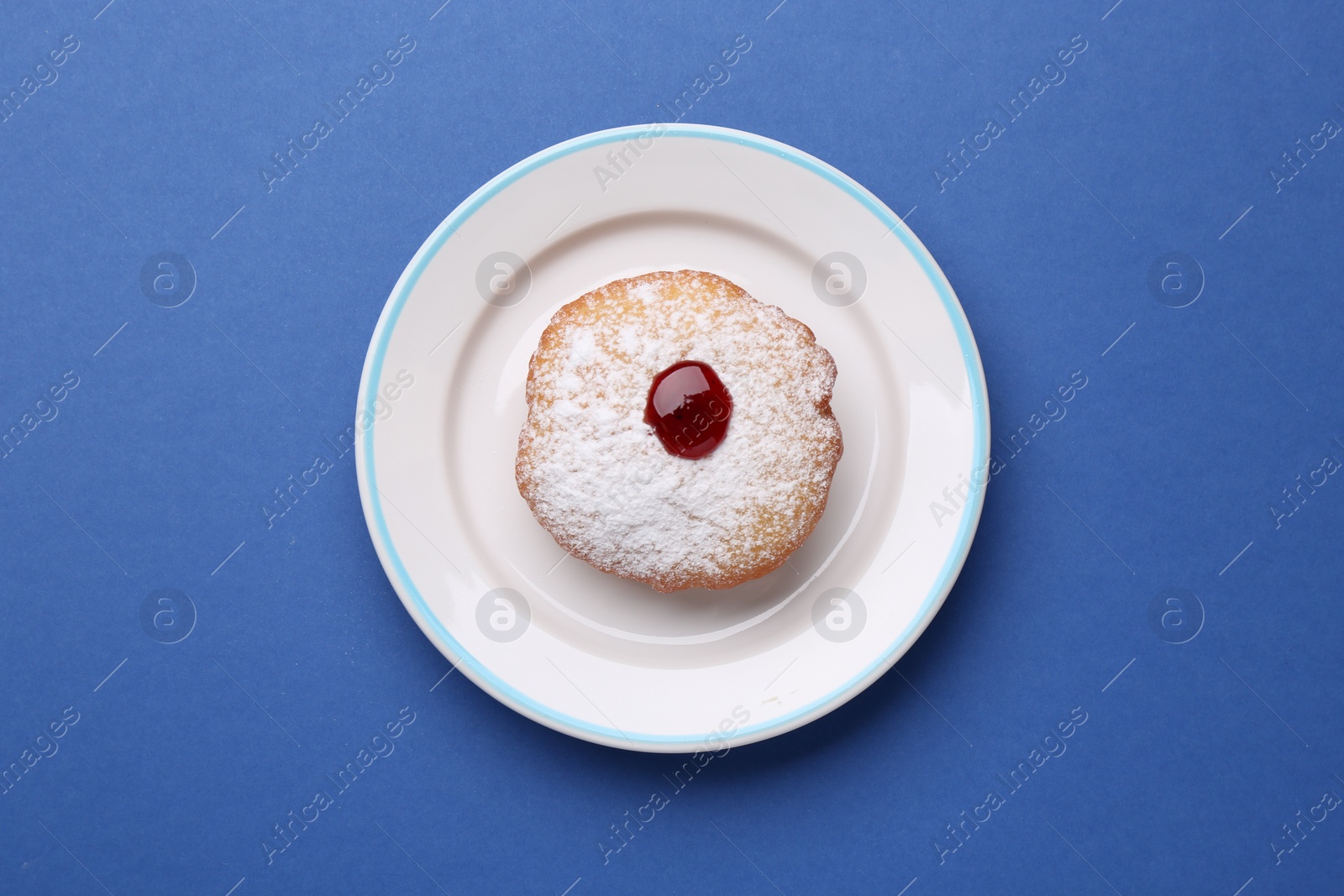 Photo of Hanukkah donut with jelly and powdered sugar on blue background, top view