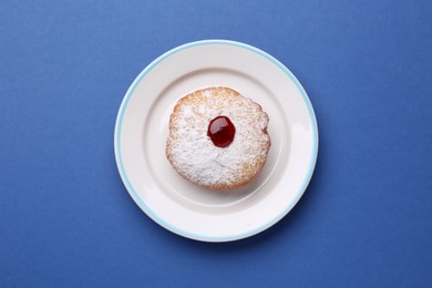 Photo of Hanukkah donut with jelly and powdered sugar on blue background, top view