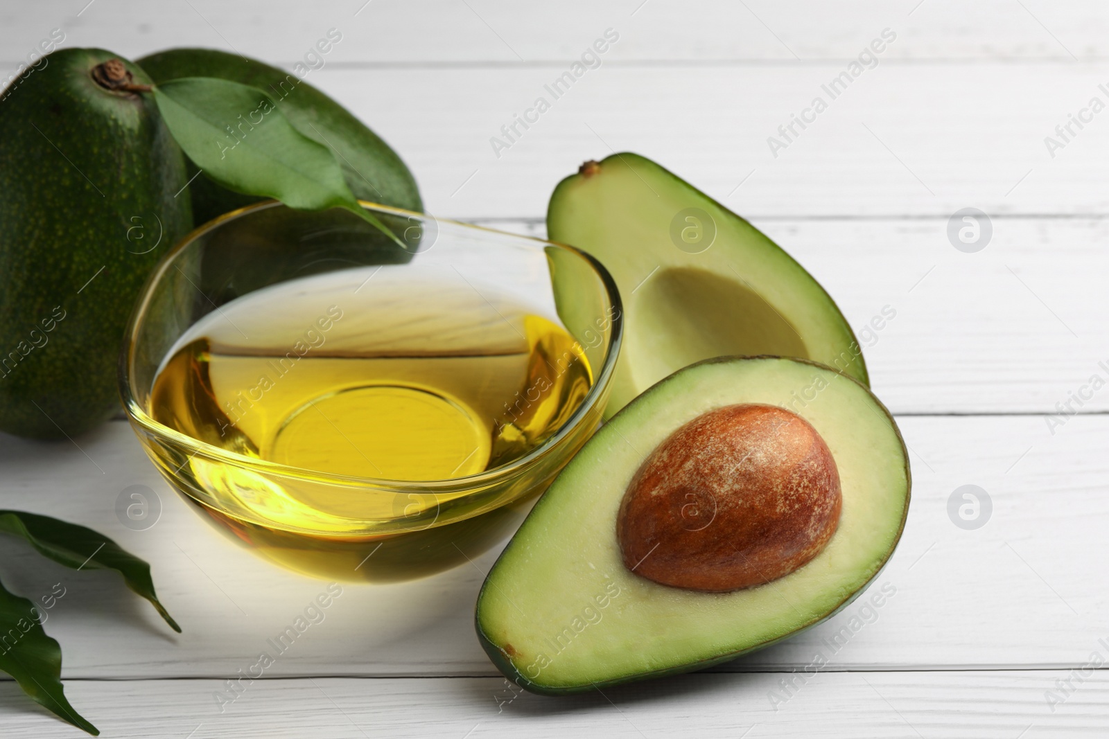 Photo of Cooking oil in bowl and fresh avocados on white wooden table