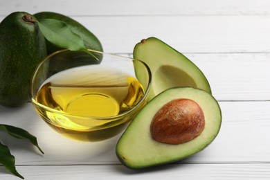 Cooking oil in bowl and fresh avocados on white wooden table