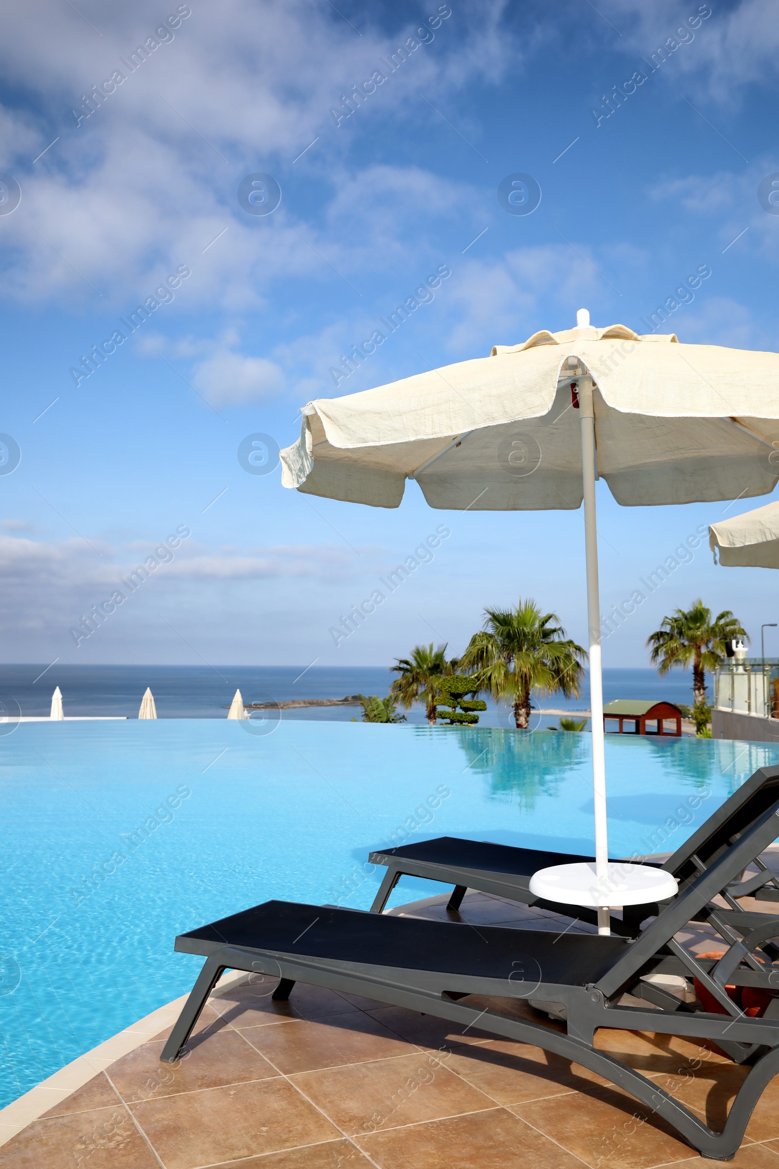 Photo of Chaise longues and beach parasol near infinity pool at resort