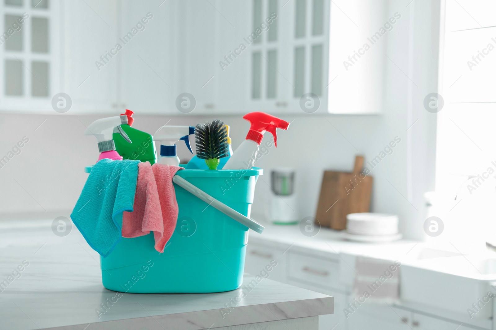 Photo of Plastic bucket with different cleaning supplies on table in kitchen. Space for text