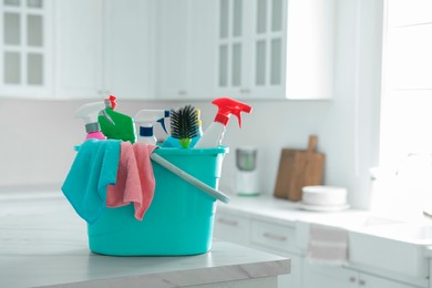 Photo of Plastic bucket with different cleaning supplies on table in kitchen. Space for text