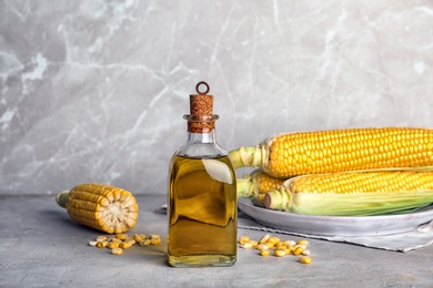 Photo of Bottle of corn oil and fresh cobs on table against light wall