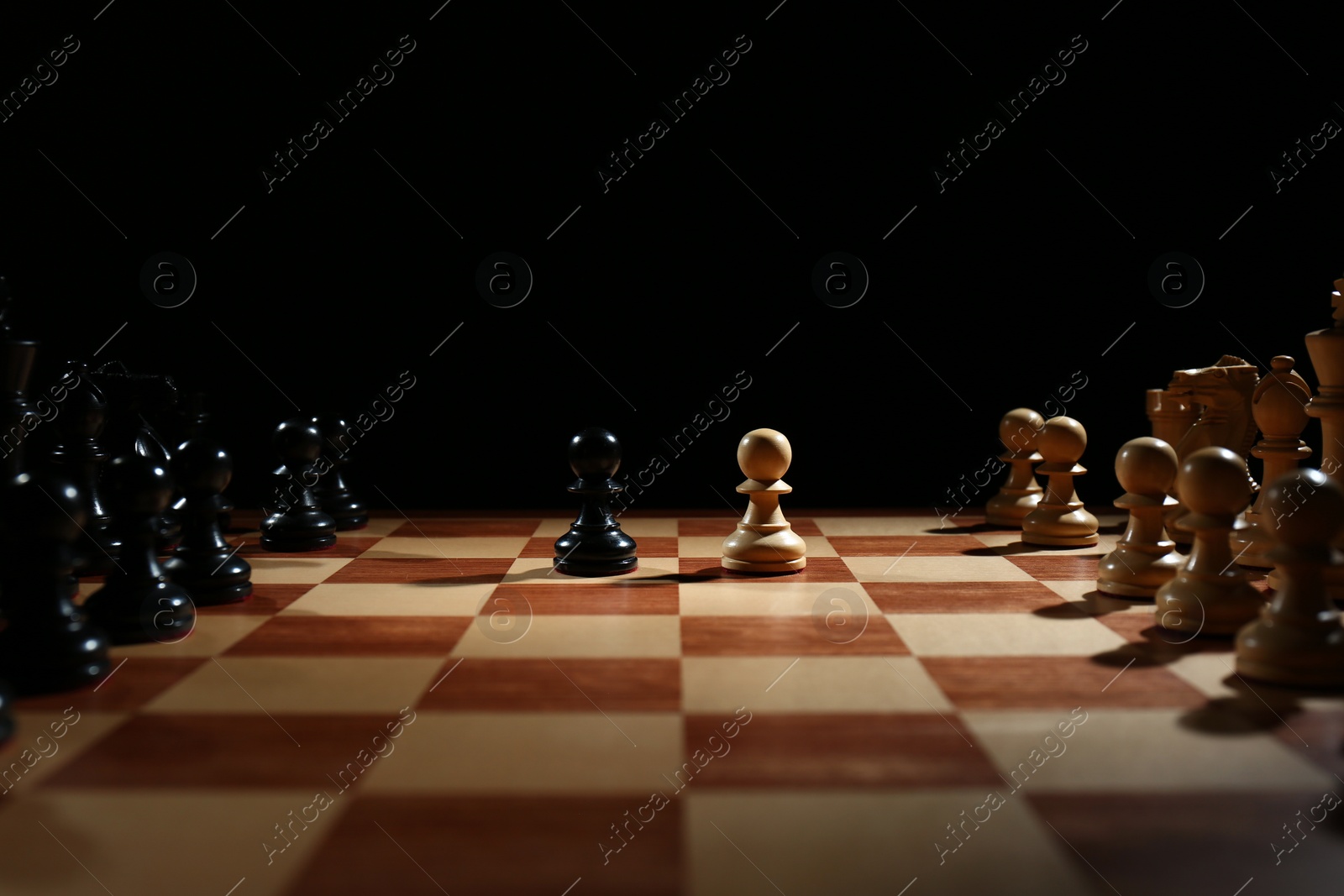 Photo of Chess pieces on wooden board against black background