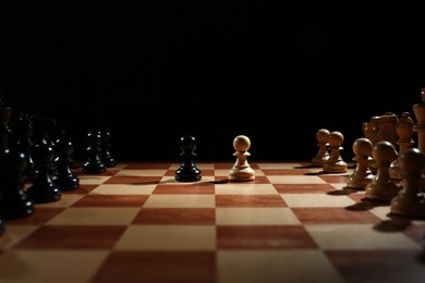 Chess pieces on wooden board against black background