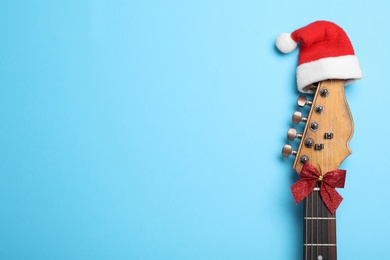 Top view of guitar with Santa hat and red bow on light blue background, space for text. Christmas music