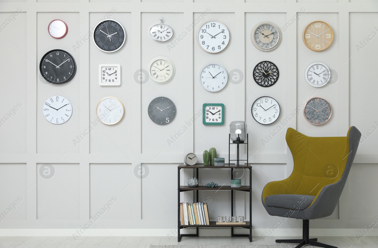 Photo of Armchair, console table and many different clocks hanging on white wall in room