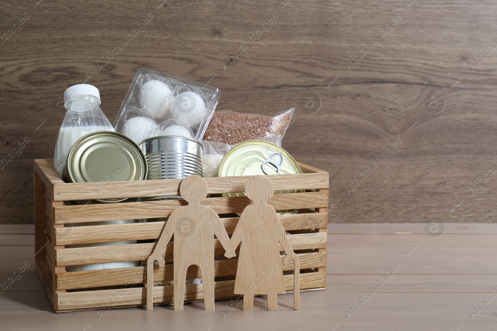 Photo of Humanitarian aid for elderly people. Donation box with food products and figure of senior couple isolated on wooden table, space for text