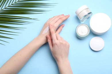 Woman applying hand cream on light blue background, top view