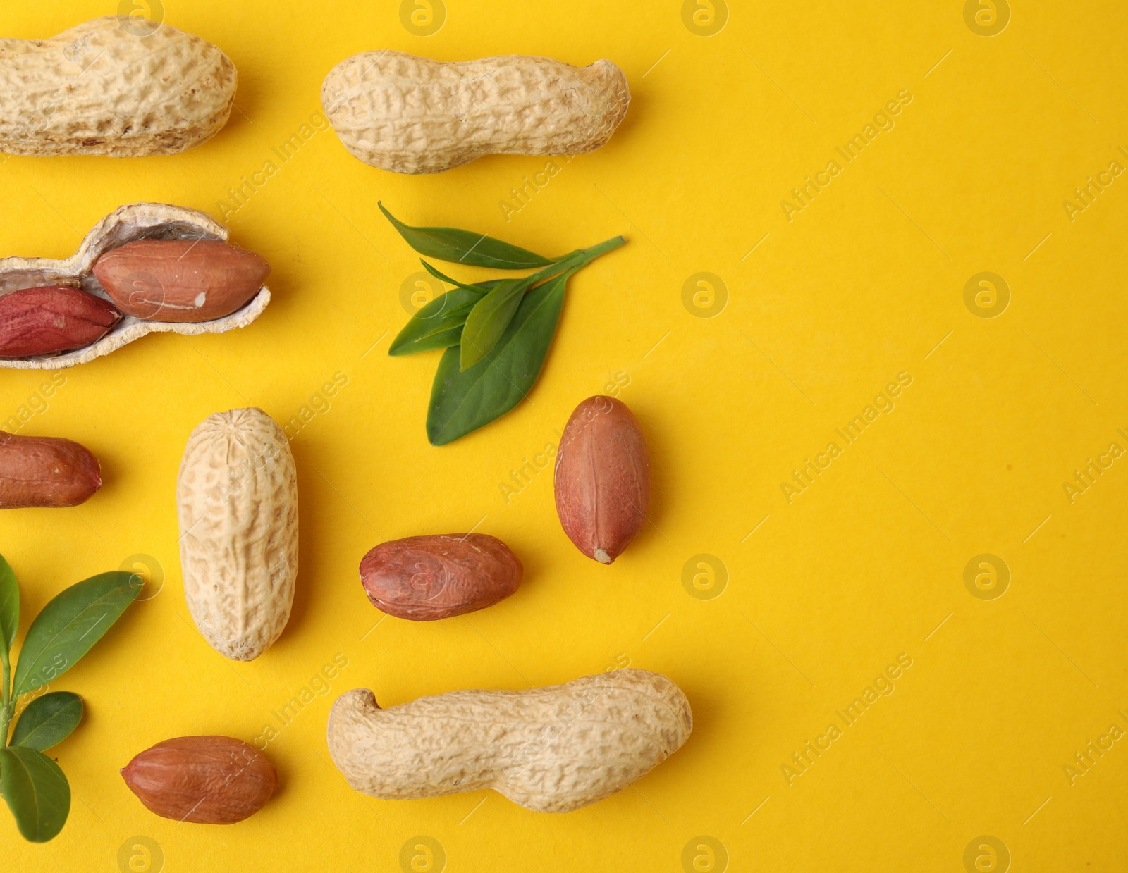 Photo of Fresh peanuts and leaves on yellow table, flat lay. Space for text