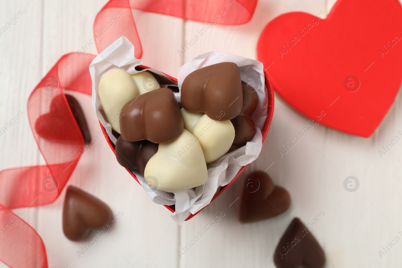 Photo of Beautiful heart shaped chocolate candies on white wooden table, flat lay