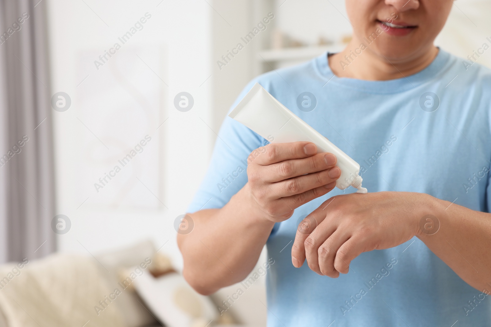 Photo of Man applying body cream onto his hand indoors, closeup. Space for text