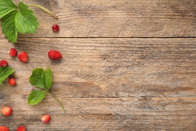 Photo of Many fresh wild strawberries and leaves on wooden table, flat lay. Space for text