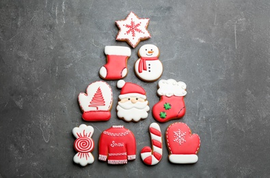 Photo of Christmas tree shape made of delicious decorated gingerbread cookies on grey table, flat lay