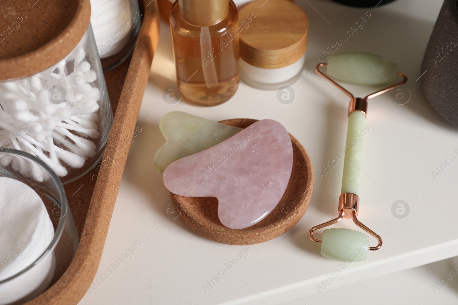 Photo of Gua sha tools, natural face roller and toiletries on white shelf