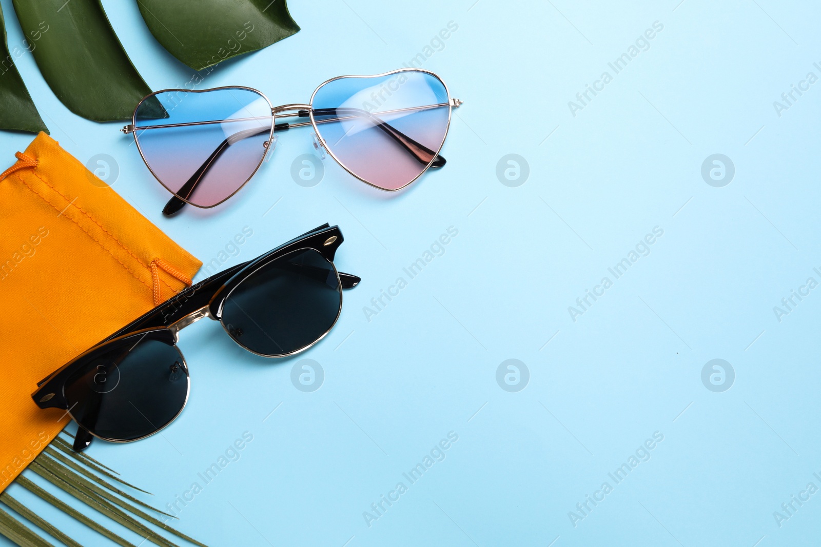 Photo of Different stylish sunglasses with bag on light blue background, flat lay. Space for text