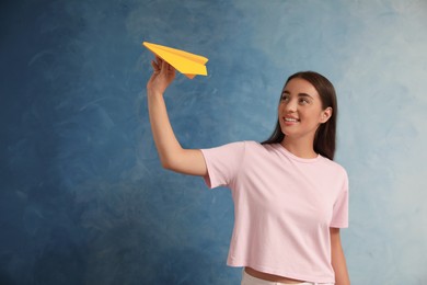 Beautiful young woman playing with paper plane on light blue background