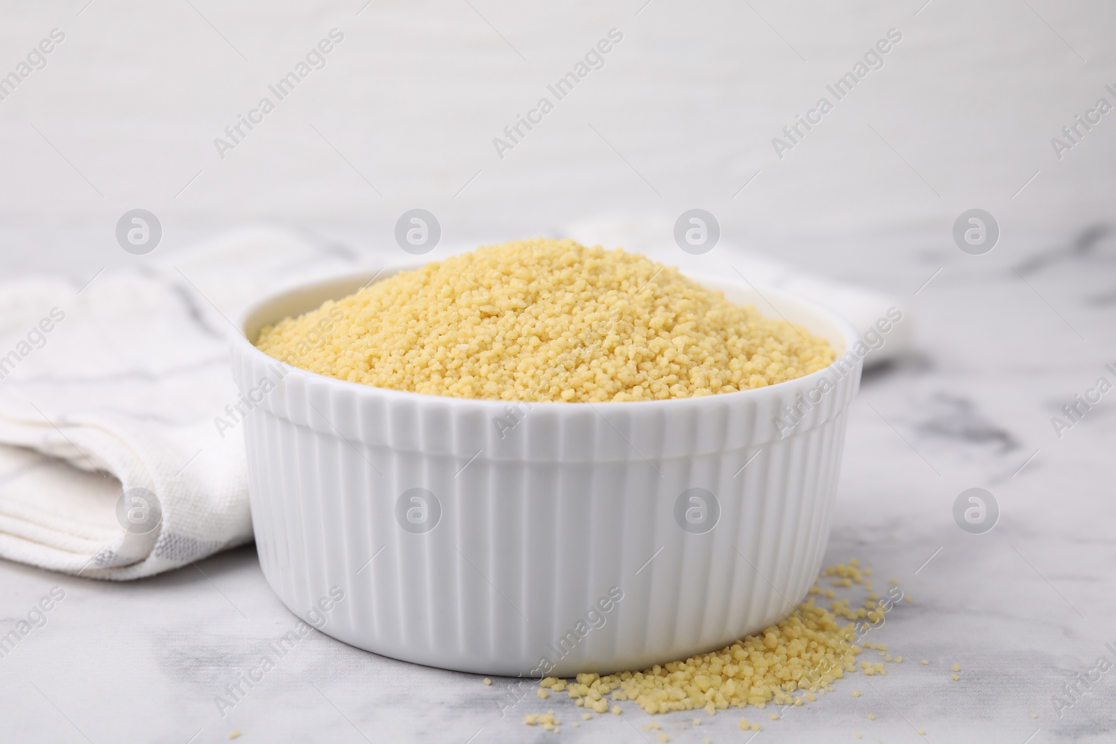 Photo of Raw couscous in bowl on light table, closeup