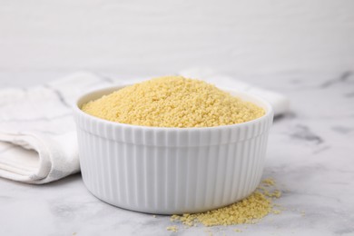 Raw couscous in bowl on light table, closeup