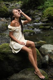 Photo of Beautiful young woman sitting on rock near mountain river outdoors