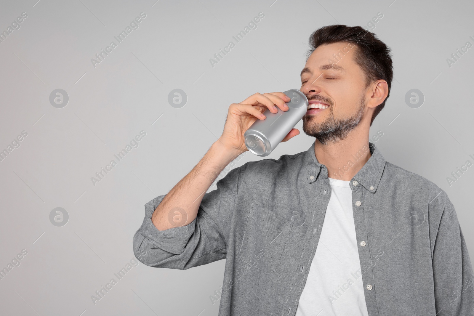 Photo of Happy man drinking from tin can on light grey background