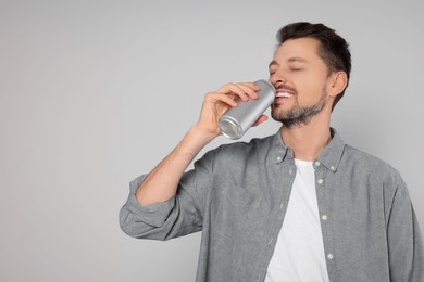 Happy man drinking from tin can on light grey background