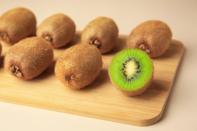 Wooden board with whole kiwis and cut one on beige background, closeup