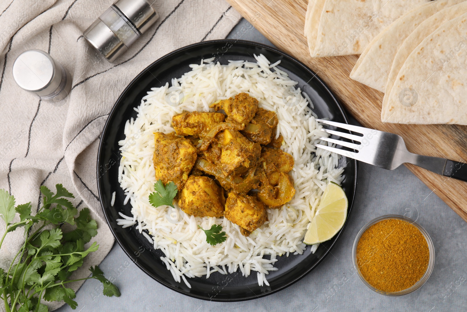 Photo of Delicious chicken curry with rice and ingredients on grey table, flat lay